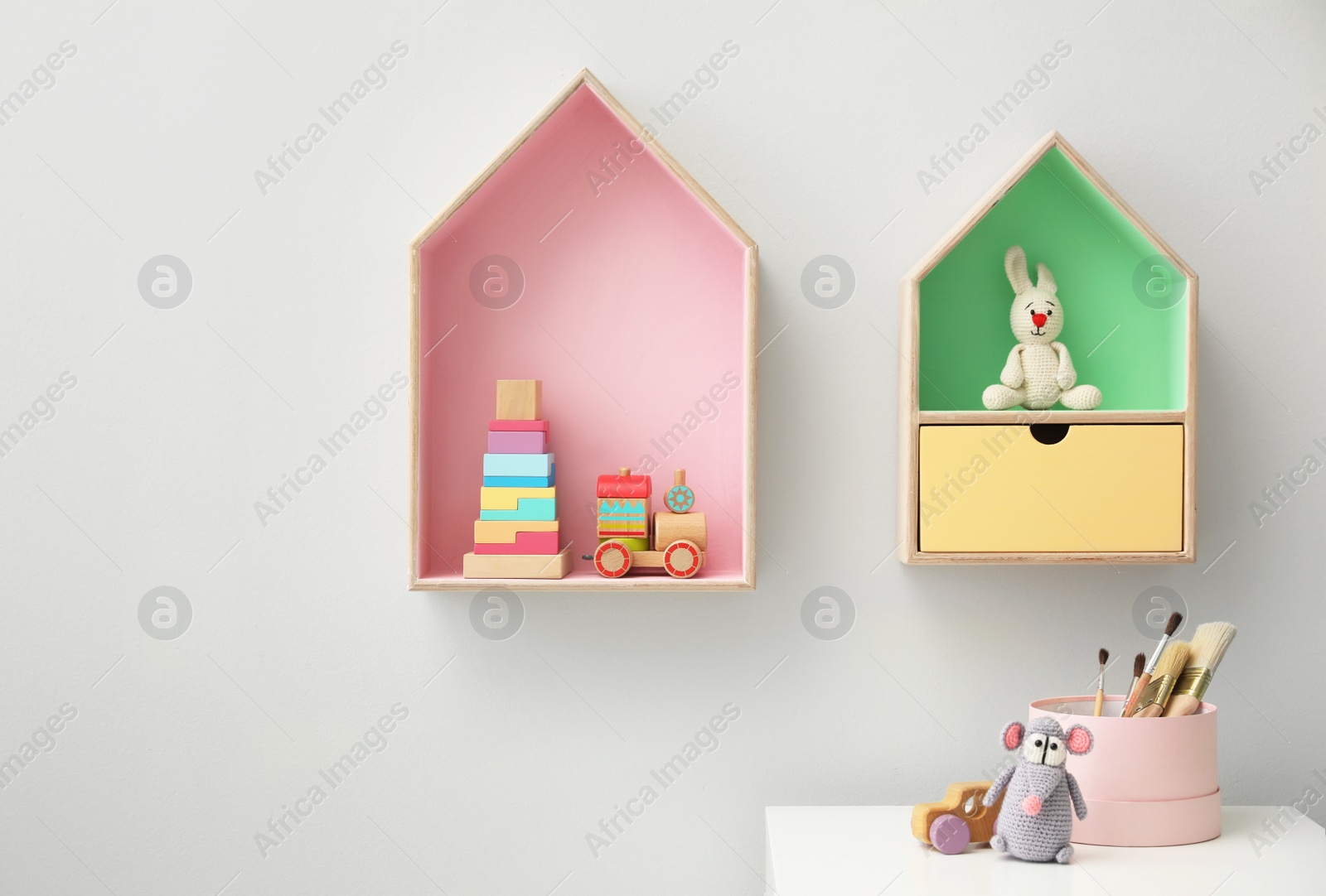 Photo of House shaped shelves and white table in children's room. Interior design