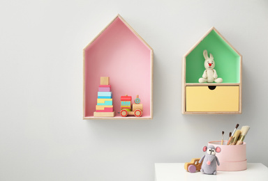 Photo of House shaped shelves and white table in children's room. Interior design