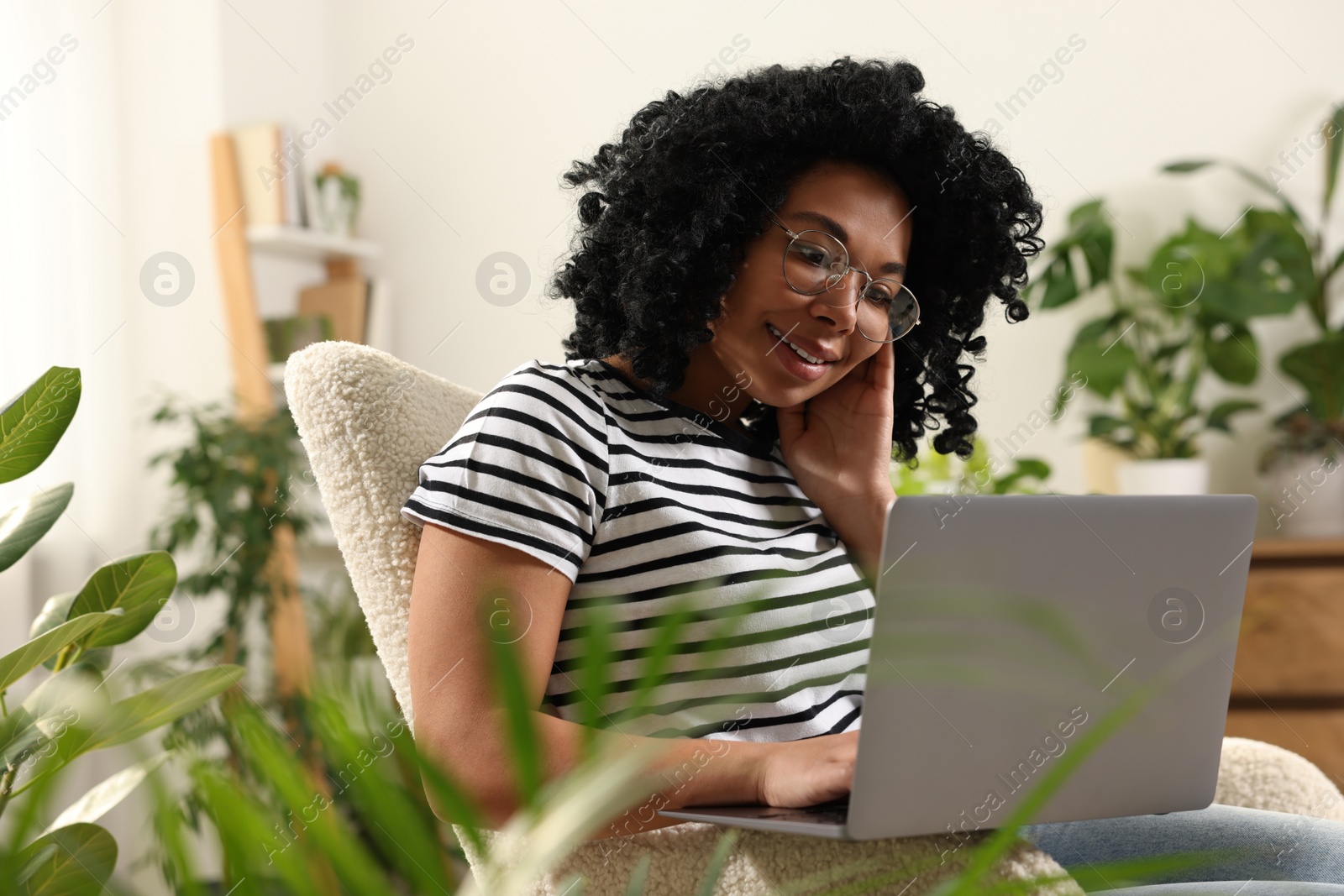 Photo of Relaxing atmosphere. Happy woman with laptop sitting in armchair surrounded by houseplants at home