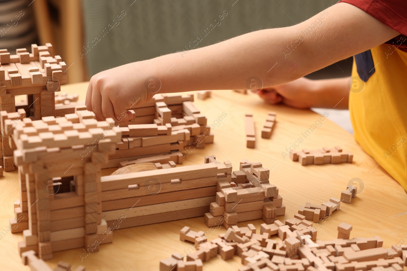 Photo of Little boy playing with wooden construction set at table indoors, closeup. Child's toy