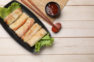 Photo of Delicious fried spring rolls, sauce and chopsticks on light wooden table, flat lay. Space for text