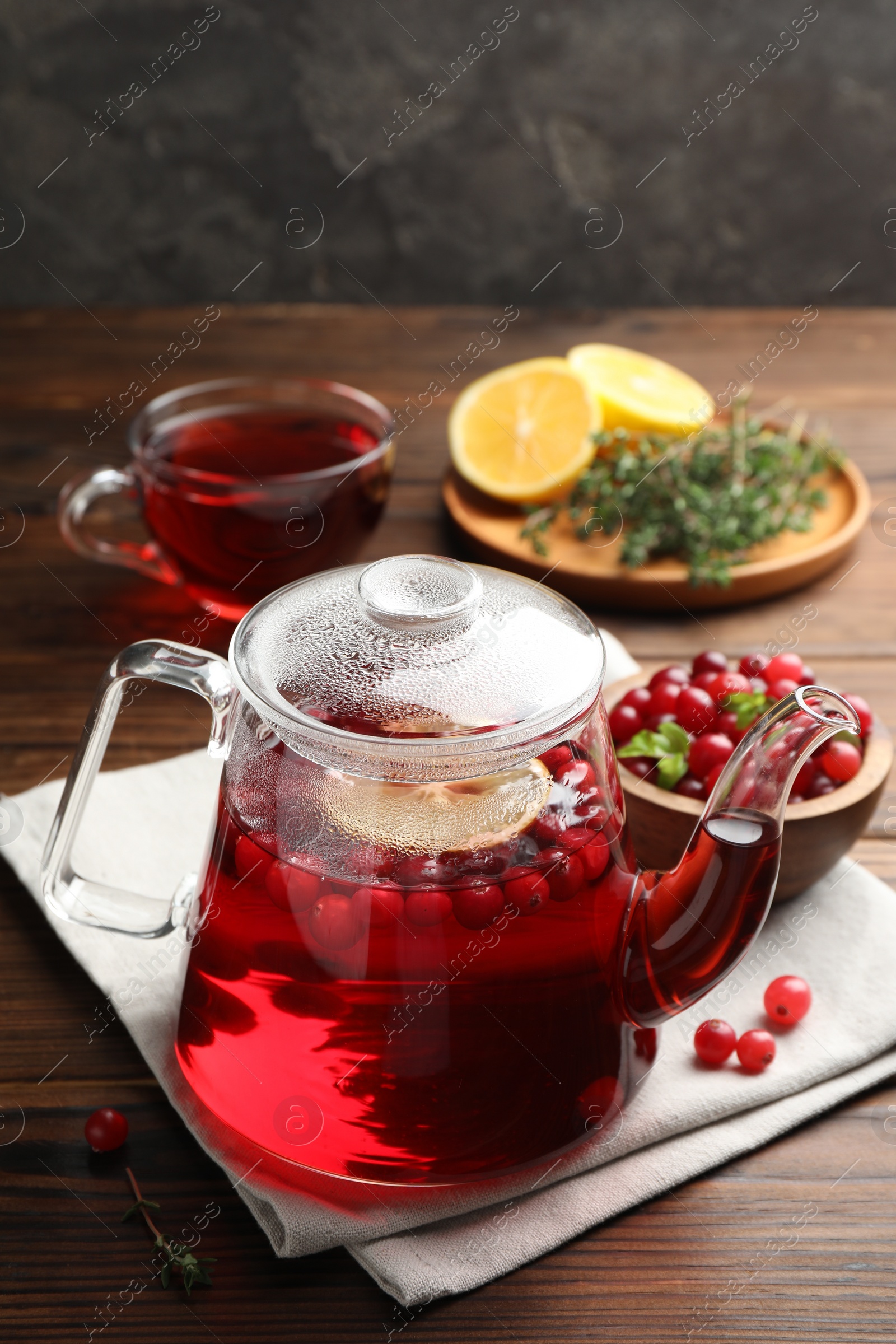 Photo of Tasty hot cranberry tea in teapot and fresh berries on wooden table