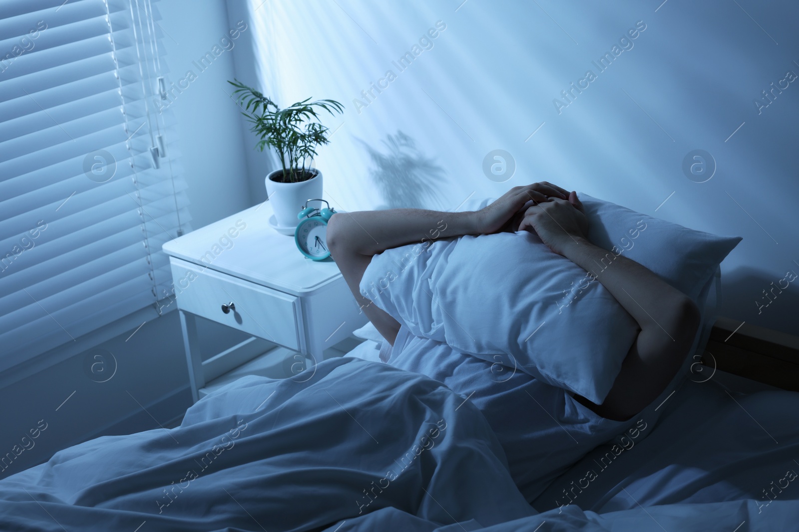 Photo of Sleepy man covering head with pillow in bed at home