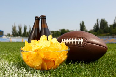 Photo of American football ball with beer and chips on green field grass in stadium