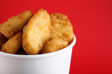 Bucket with delicious chicken nuggets on red background, closeup