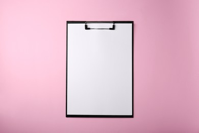 Photo of Black clipboard with sheet of blank paper on pink background, top view