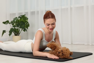 Young woman practicing yoga on mat with her cute dog indoors