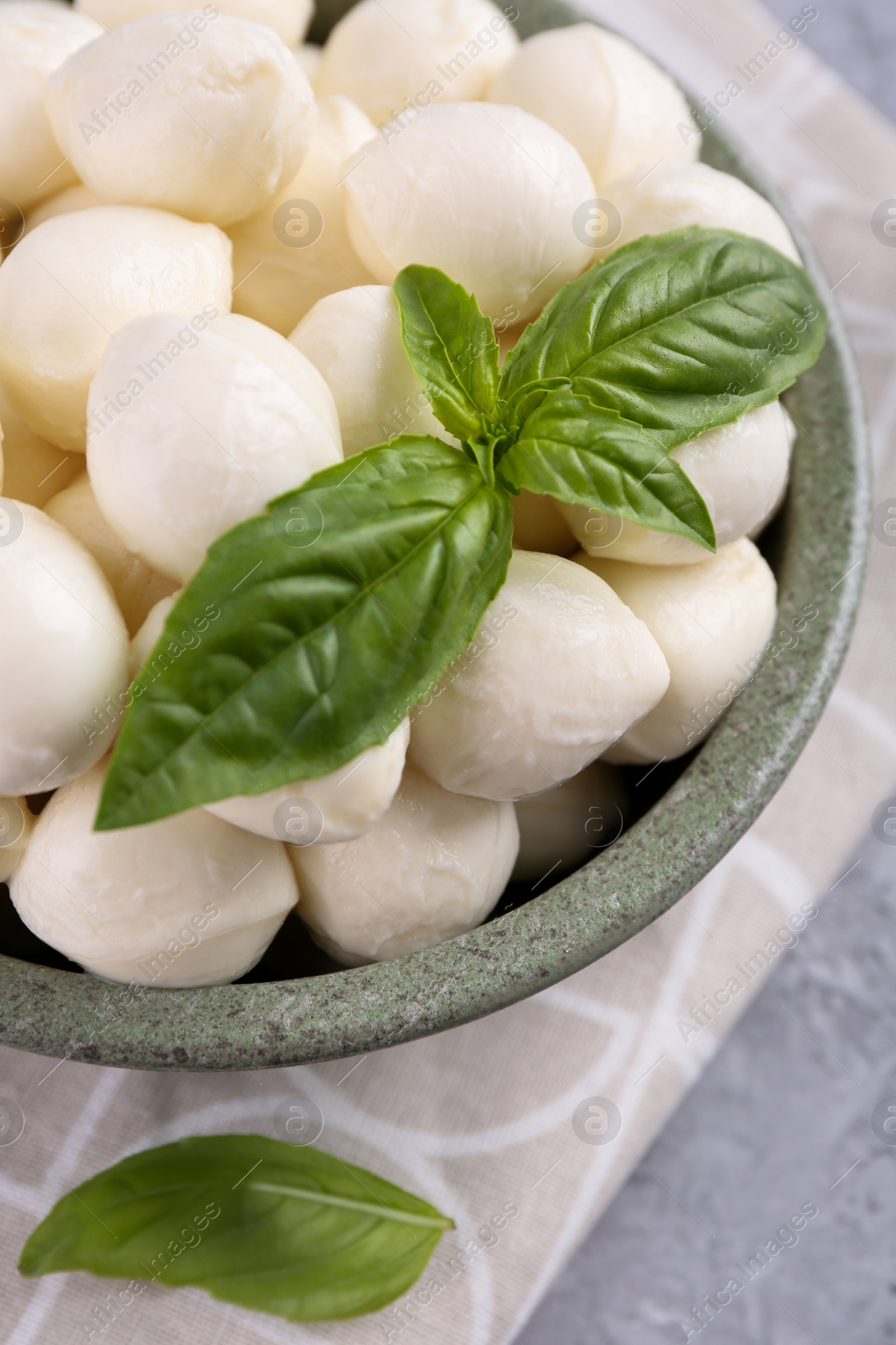 Photo of Tasty mozzarella balls and basil leaves in bowl on grey table, closeup