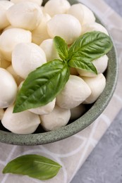 Photo of Tasty mozzarella balls and basil leaves in bowl on grey table, closeup