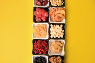 Bowls with dried fruits and nuts on yellow background, flat lay