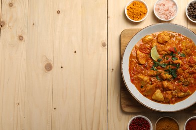 Delicious chicken curry and spices on wooden table, flat lay. Space for text