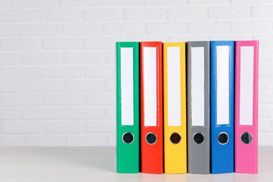 Many hardcover office folders on wooden table near white brick wall, space for text