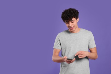 Photo of Handsome young man using smartphone on violet background. Space for text
