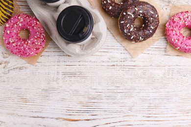 Tasty donuts and cup of hot drink on white wooden table, flat lay. Space for text