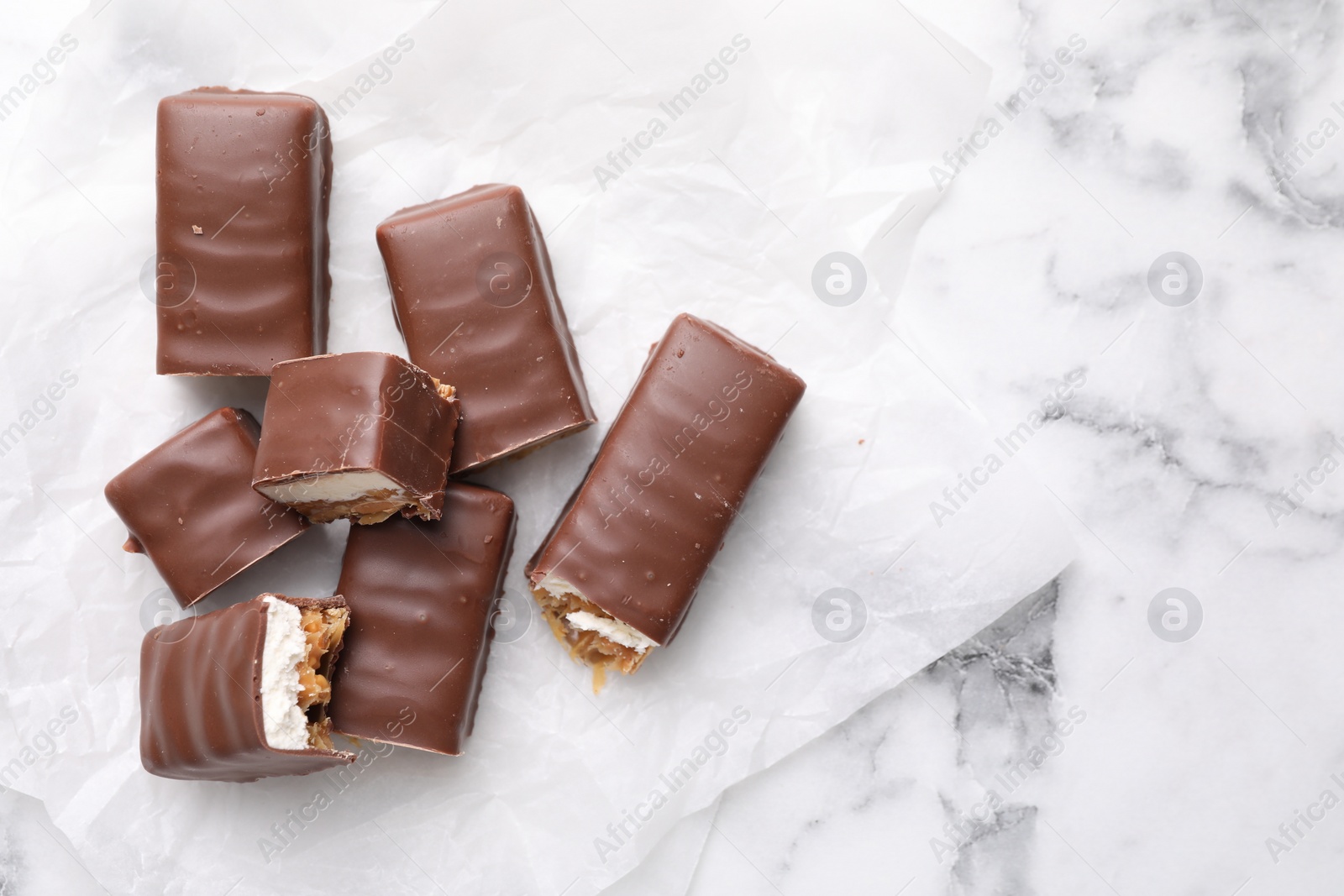 Photo of Tasty chocolate bars with nougat on white marble table, top view. Space for text