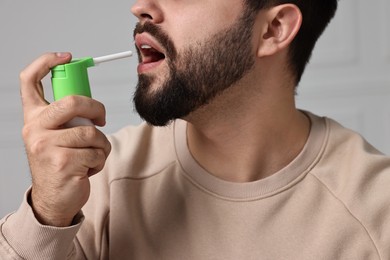 Young man using throat spray indoors, closeup