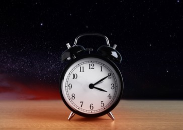 Image of Alarm clock on wooden table against night sky with stars. Insomnia