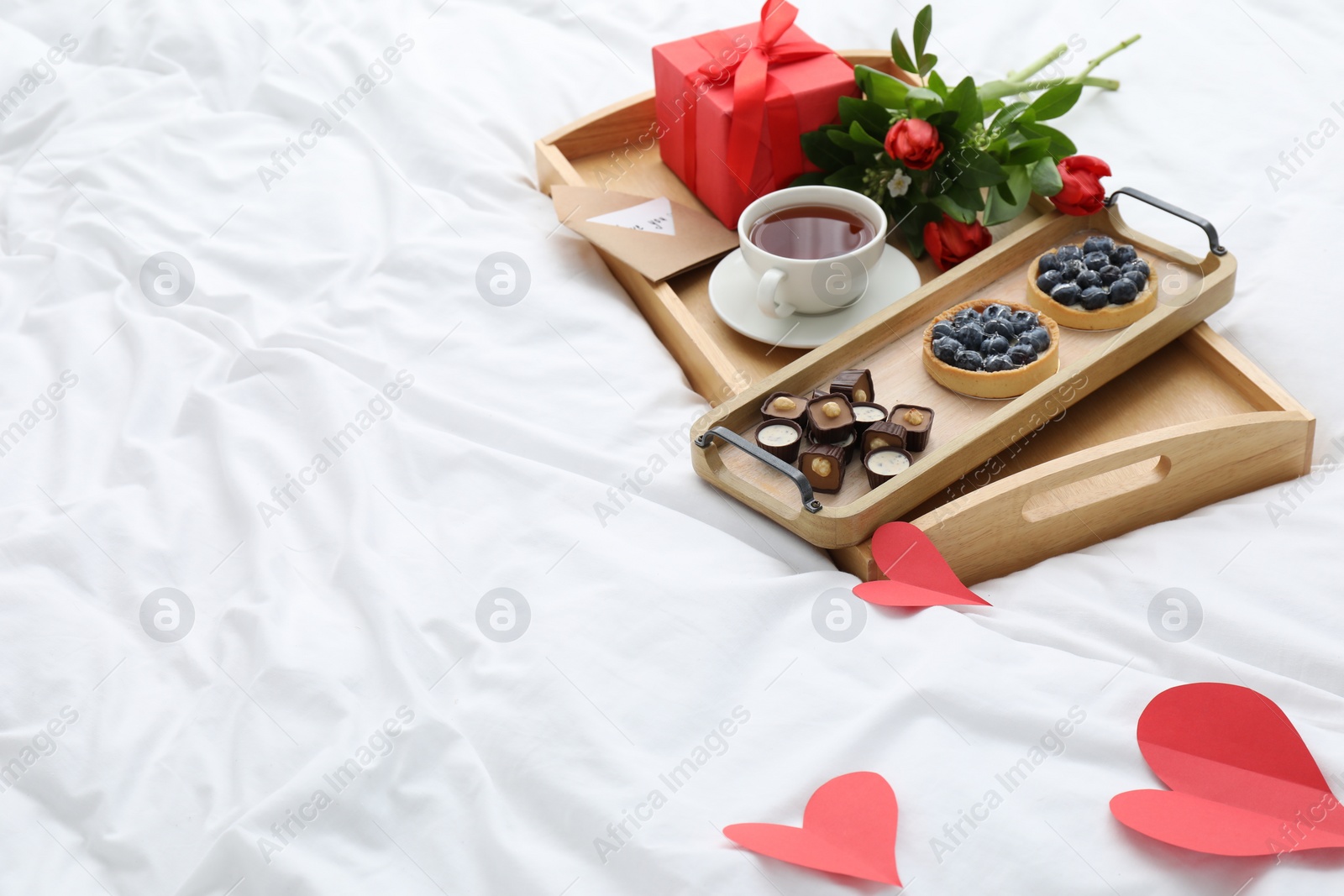 Photo of Tasty breakfast served in bed. Delicious desserts, tea, flowers and gift box on tray, space for text