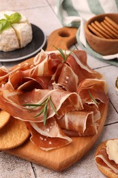 Photo of Slices of tasty cured ham, crackers and rosemary on tiled table, closeup