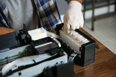 Photo of Professional repairman fixing modern printer indoors, closeup