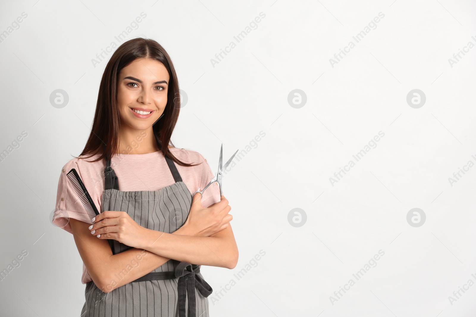 Photo of Young hairstylist holding professional scissors and comb on light background