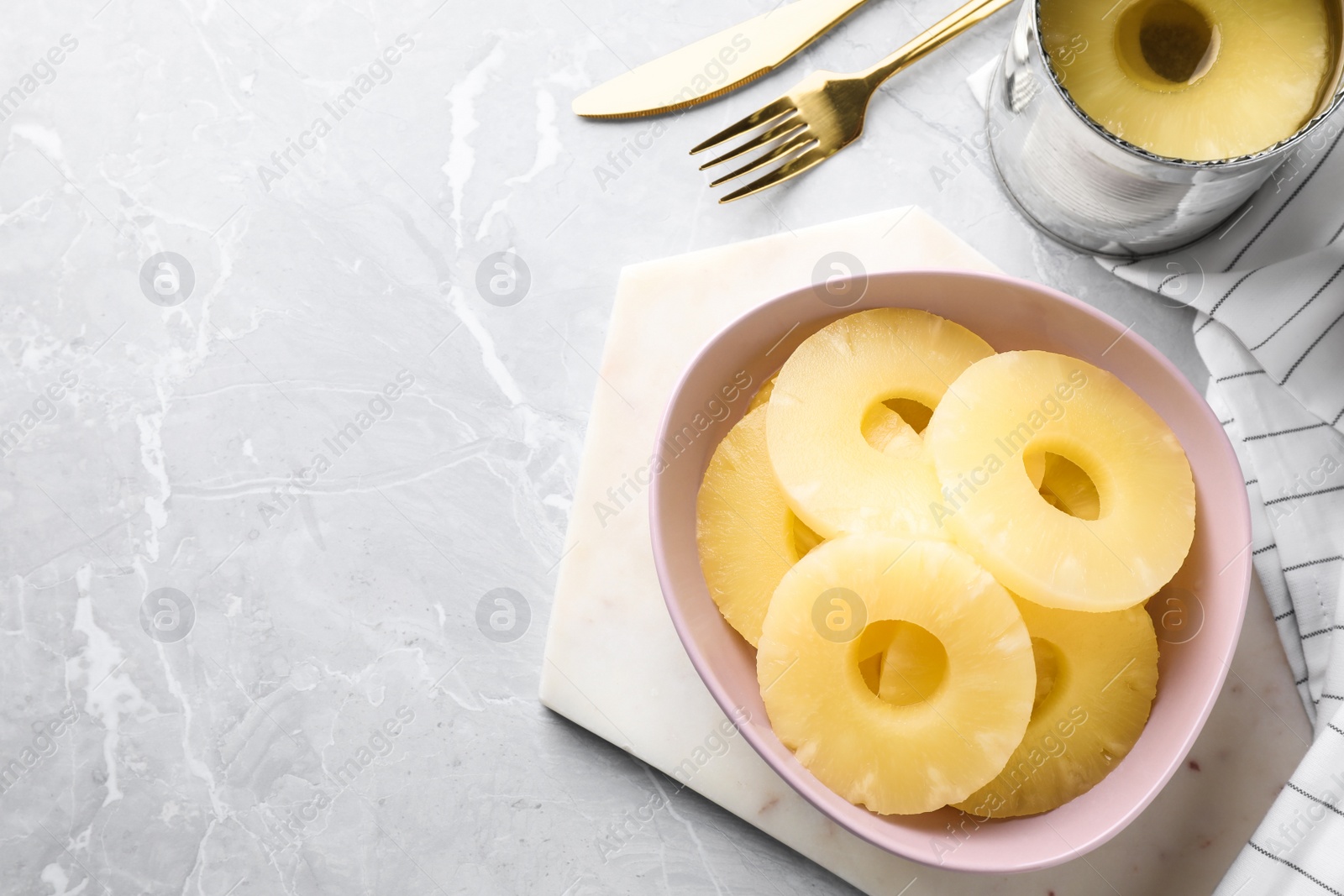 Photo of Delicious canned pineapple in bowl on light grey marble table, above view. Space for text