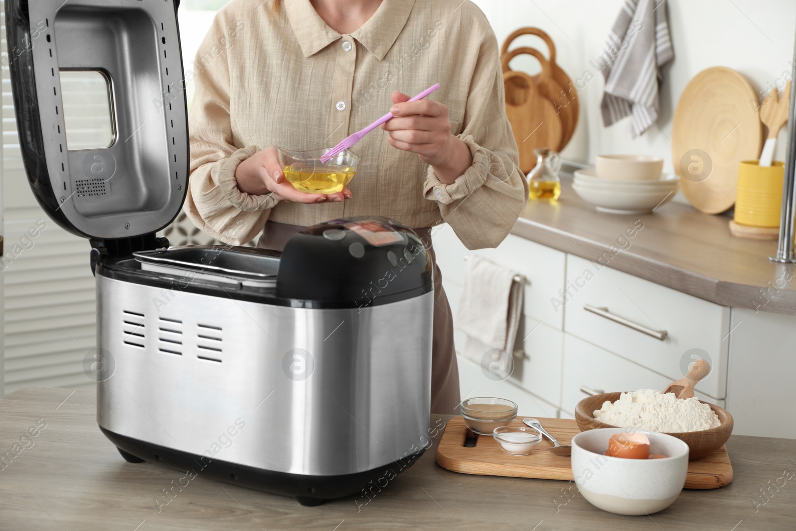 Photo of Woman with oil near breadmaker at wooden table in kitchen, closeup