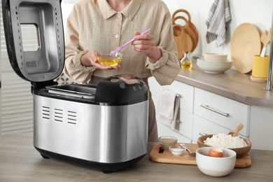 Photo of Woman with oil near breadmaker at wooden table in kitchen, closeup