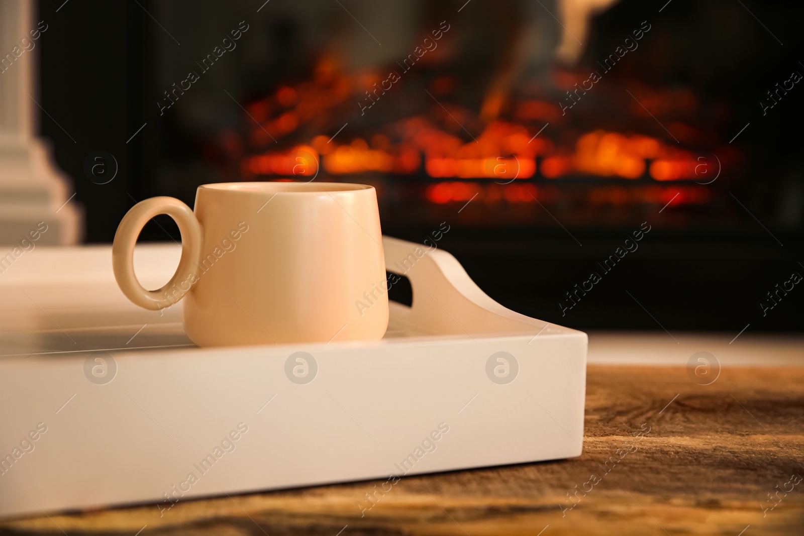 Photo of Cup with hot drink in tray on wooden table against fireplace, space for text