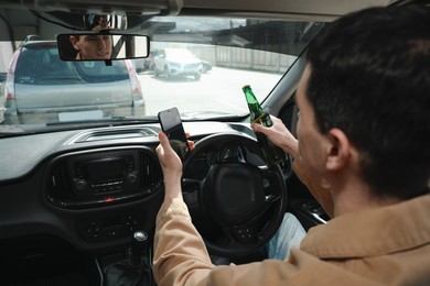 Man with bottle of beer and smartphone in car. Don't drink and drive concept