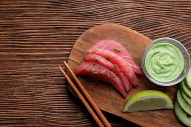 Photo of Tasty sashimi (pieces of fresh raw tuna) served with wasabi sauce and lime wedge on wooden table, top view