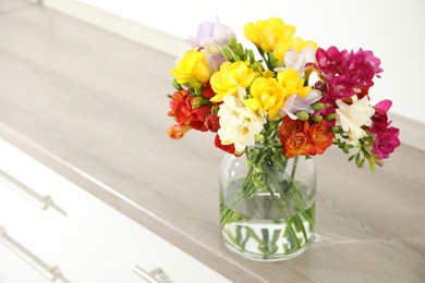 Photo of Beautiful bright spring freesia flowers in vase on chest of drawers. Space for text