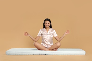 Young woman meditating on soft mattress against beige background