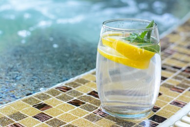 Photo of Refreshing water with lemon and mint on edge of swimming pool, space for text