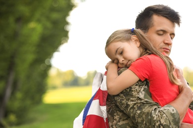 Father in military uniform with American flag hugging his daughter at sunny park