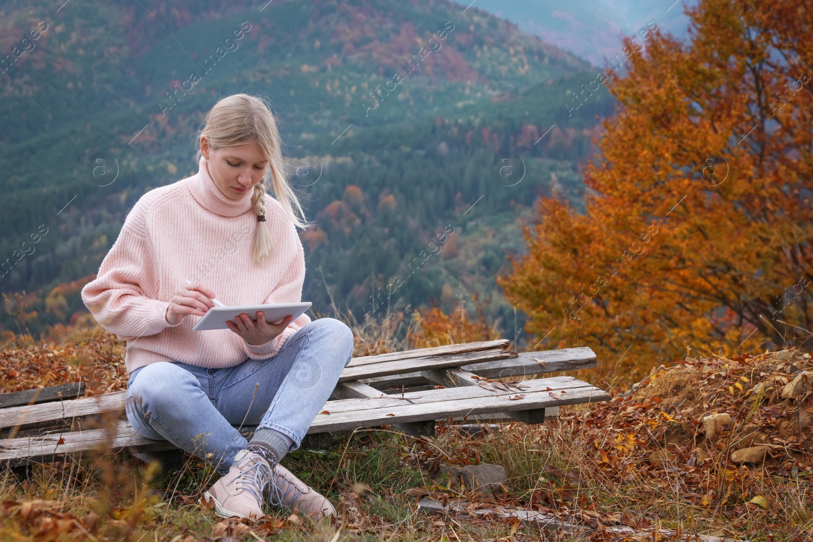 Photo of Young woman drawing on tablet in mountains, space for text