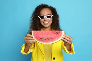 Beautiful young African American woman with watermelon against light blue background, focus on hands