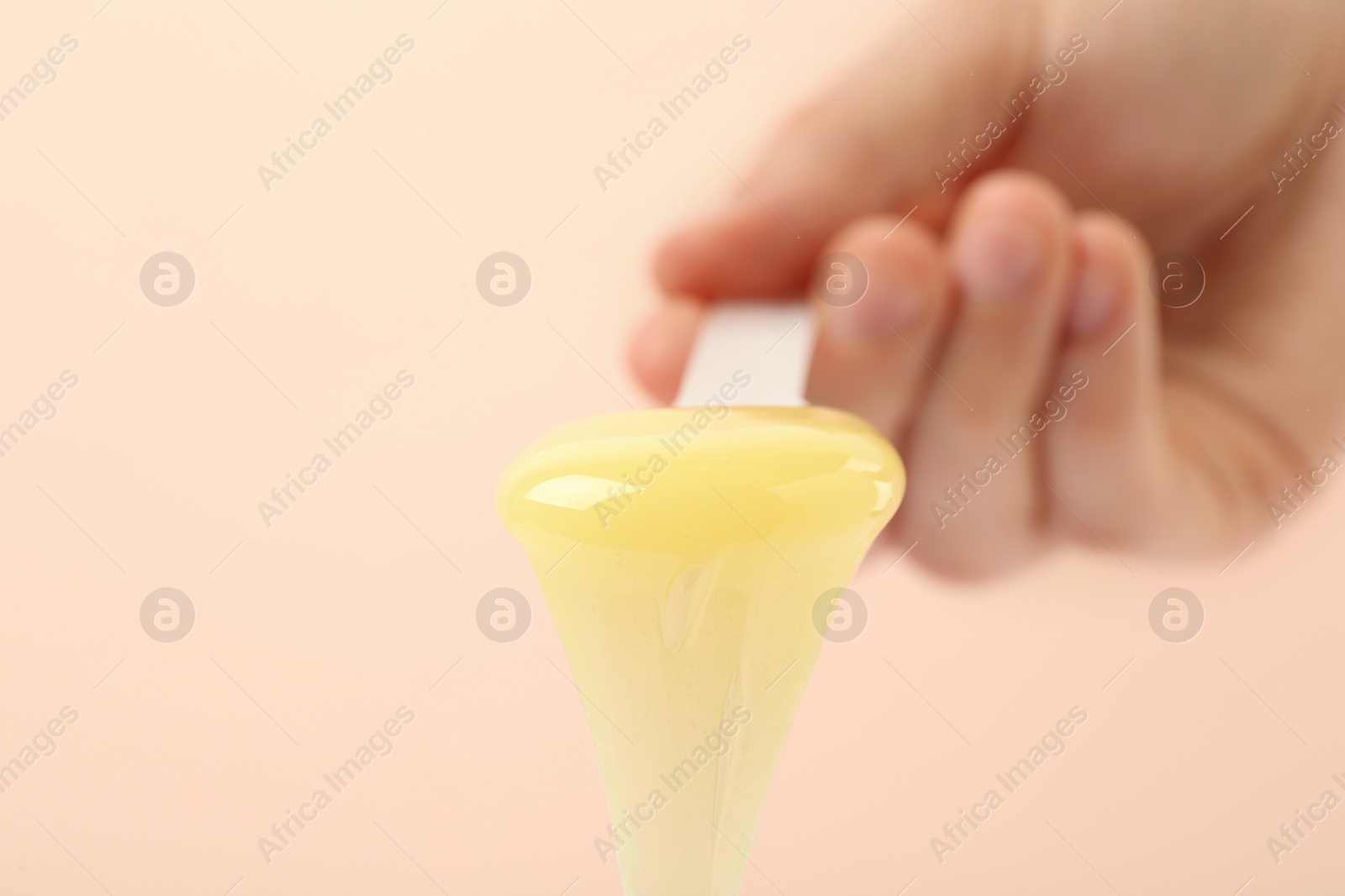 Photo of Woman holding spatula with hot depilatory wax on beige background, closeup. Space for text