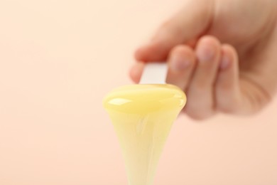 Woman holding spatula with hot depilatory wax on beige background, closeup. Space for text