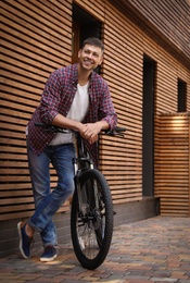 Handsome man with modern bicycle near building outdoors