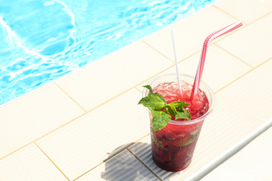 Delicious refreshing drink in plastic cup near swimming pool. Space for text