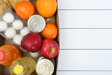 Humanitarian aid. Different food products for donation in box on white wooden table, top view. Space for text