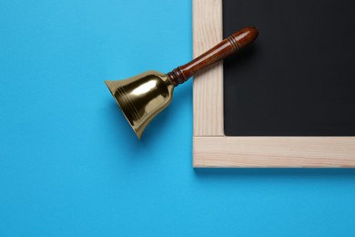 Photo of Golden bell and blackboard on light blue background, flat lay. School days