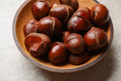 Fresh edible sweet chestnuts in wooden bowl on grey table, closeup