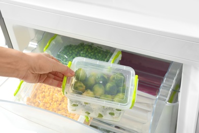 Photo of Woman taking container with frozen brussel sprouts from refrigerator, closeup