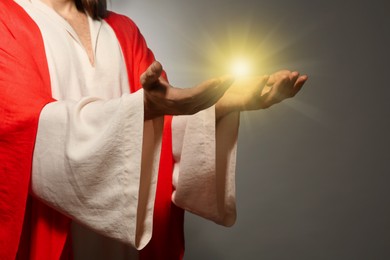 Image of Jesus Christ on grey background, closeup. Miraculous light in hands