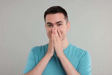 Photo of Embarrassed man covering mouth with hands on grey background