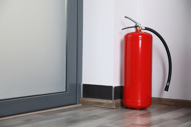 Photo of Fire extinguisher near door indoors. Space for text