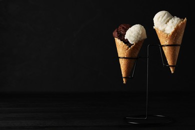 Photo of Ice cream scoops in wafer cones on black wooden table against dark background, space for text