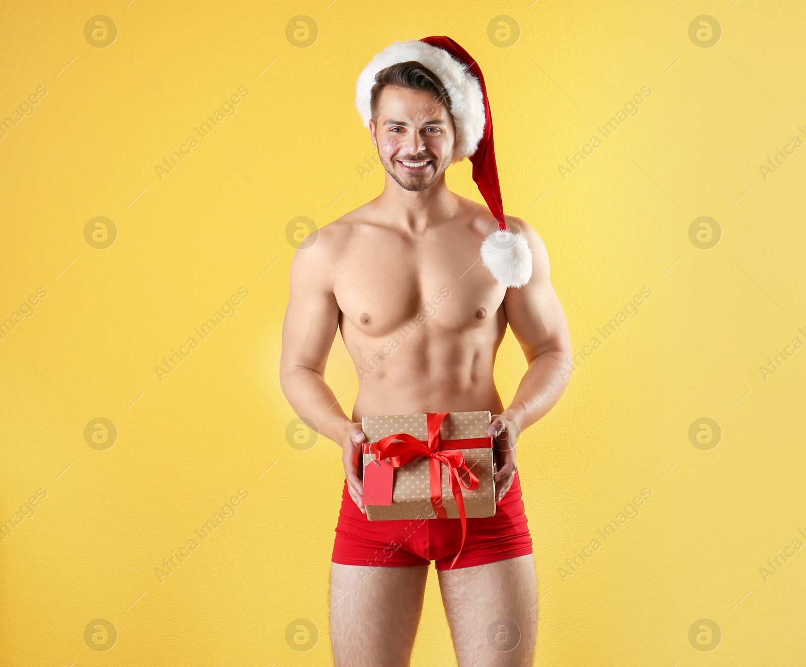 Photo of Shirtless sexy young Santa Claus with gift on color background